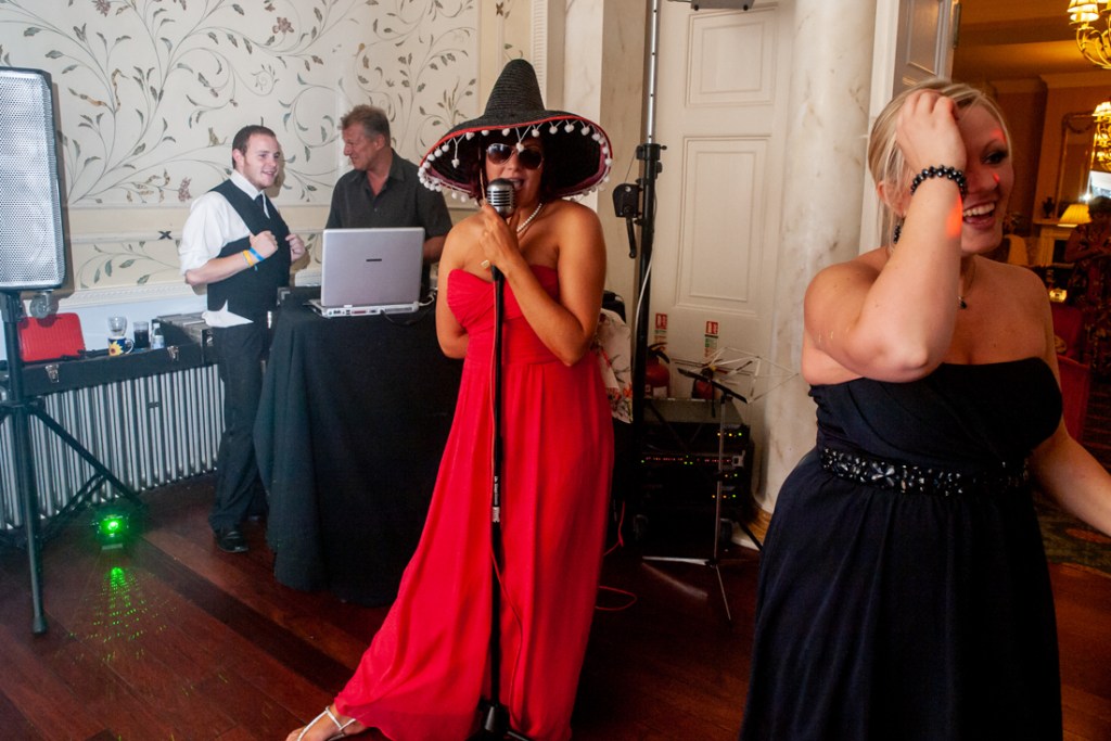A bridesmaid wearing a sombrero sings during the evening reception, at Shropshire wedding venue, Rowton Castle. 