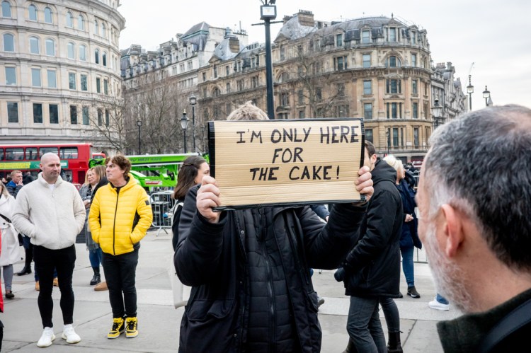 A man holds up a sign saying he is only here for the cake in Trafalgar Square, London.