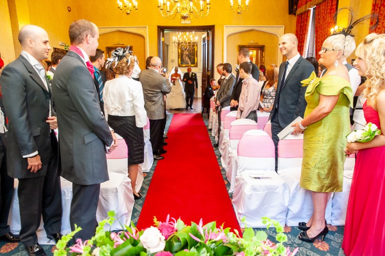 The groom looks on as the bride, and her father, come up the aisle during a wedding at Rowton Castle in Shropshire.
