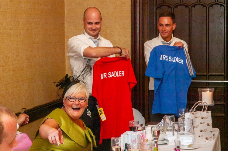 The Best Men hold up football shirts, as the mother-of-the-bride laughs and points, during the speeches at a wedding at Rowton Castle in Shropshire.