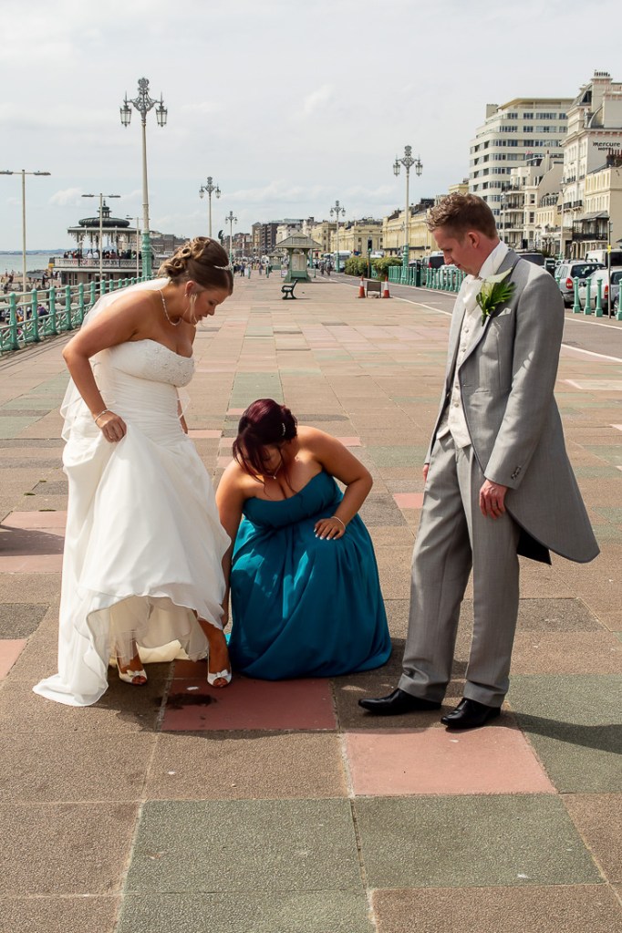 The bride is helped with her shoes on the seafront, during a wedding at the Holiday Inn Seafront hotel in Brighton, East Sussex.
