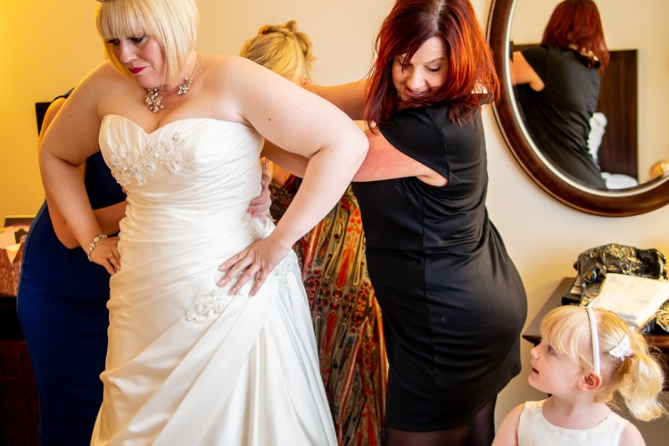 THe flower girl looks on as the bride is helped with her dress, ahead of a wedding at the Meon Valley Hotel, near Southampton, in Hampshire.