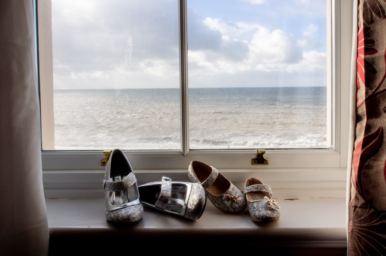Flower girls shoes in a window, with the English channel beyond, before a wedding at the Old Ship Hotel in Brighton, East Sussex.