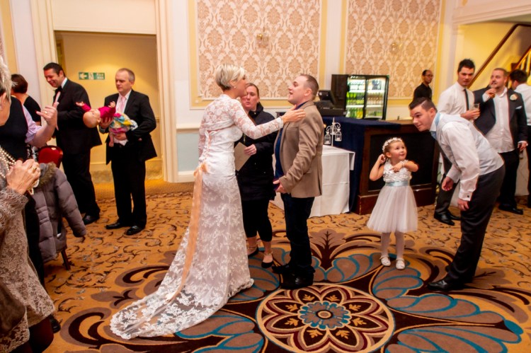 The bride with wedding guests, as the groom looks on, during the evening wedding reception at the Old Ship Hotel in Brighton, East Sussex.