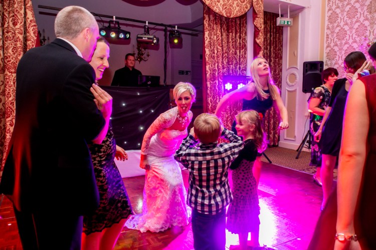 The bride sticks her toungue out at a young guest with a camera, on the dancefloor, during the evening wedding reception at the Old Ship Hotel in Brighton, East Sussex.