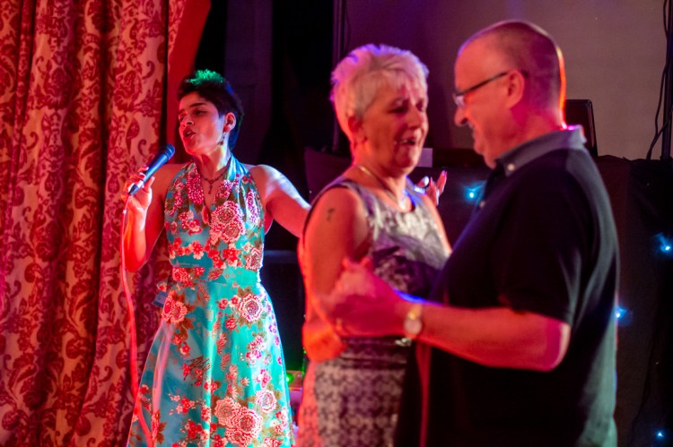 A couple dance as the wedding singer performs in the background, during the evening wedding reception at the Old Ship Hotel in Brighton, East Sussex.