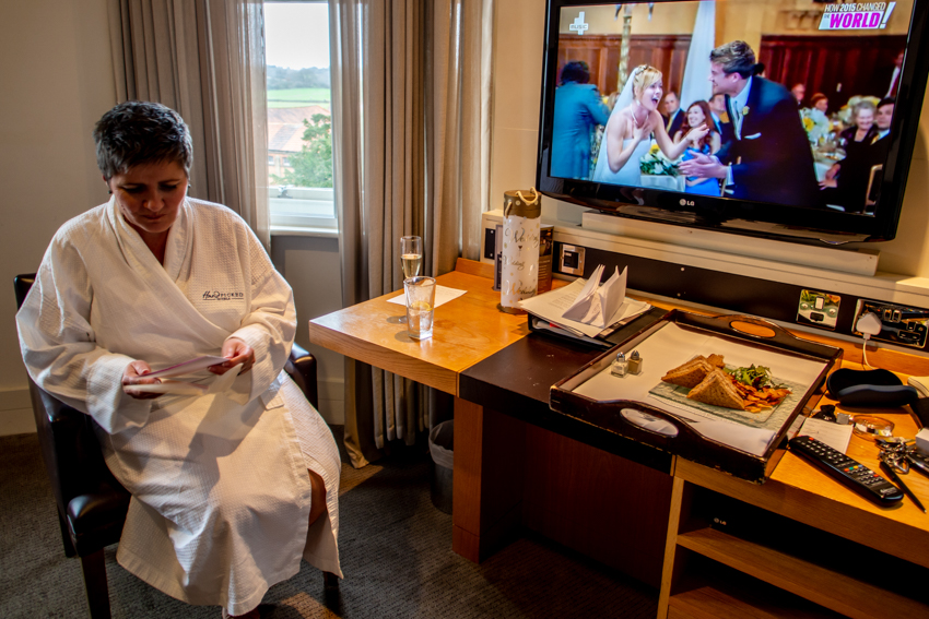 The bride reads a card, as a wedding is on TV, ahead of a real wedding at the Woodlands Park Hotel, Surrey. Taken by Bristol wedding photographer, Darren Lehane.