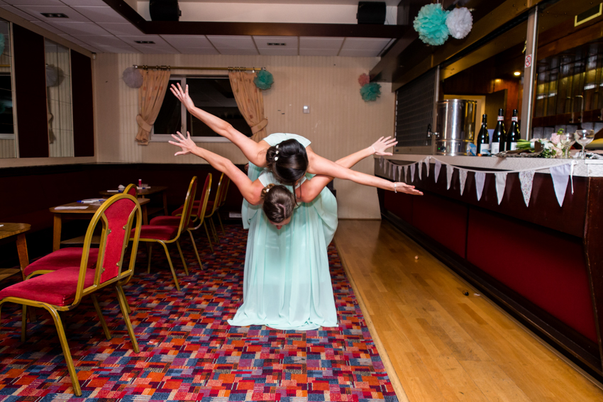 Natural wedding photography of two bridesmaids playing around during a wedding at the Holy Ghost in Luton, Bedfordshire. Taken by Bristol wedding photographer, Darren Lehane.