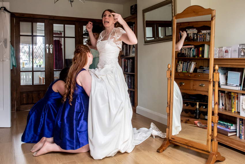 Wedding photojournalism of bridesmaids helping the bride with her dress, ahead of a wedding at Littleton Park House in Surrey. Taken by Bristol wedding photographer, Darren Lehane.