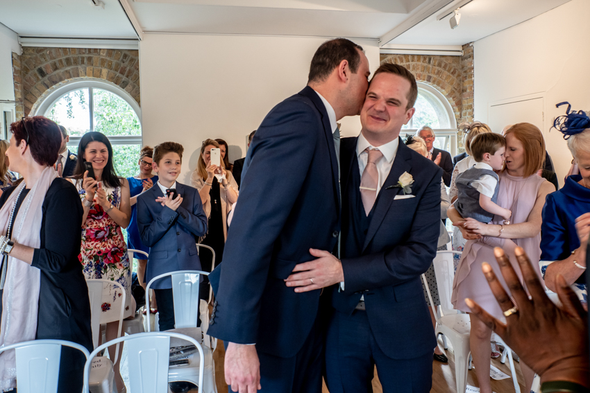 Documentary wedding photography of the grooms' first kiss during an LGBTQ+ wedding at the Pump House in Battersea Park, London. Taken by Bristol wedding photographer, Darren Lehane.