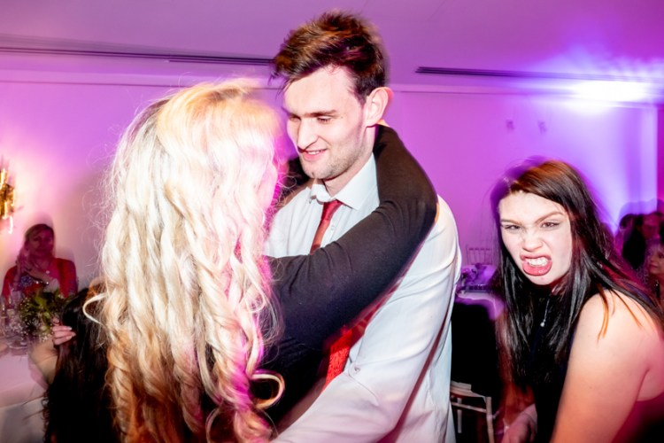 Candid street photography of a couple dancing with another gurning behind, at a wedding at the Bear Hotel in Cowbridge. Taken by Bristol wedding photographer, Darren Lehane.