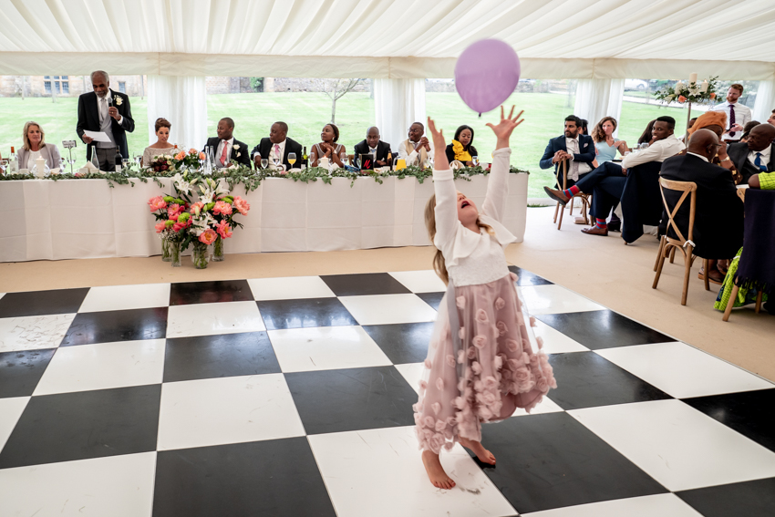 Documentary wedding photography of a girl reaching for a balloon during the wedding speeches at Ashby Manor House in Warwickshire. Taken by Bristol wedding photographer, Darren Lehane.