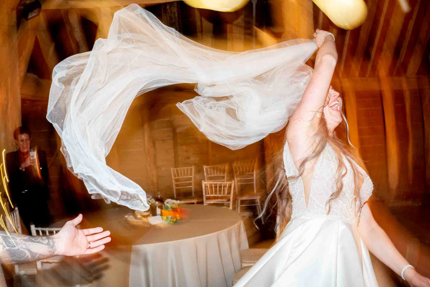 Wedding photojournalism of the bride dancing and waving her veil about during a wedding at the Priory in Little Wymondley, Herts. Taken by Bristol wedding photographer, Darren Lehane.