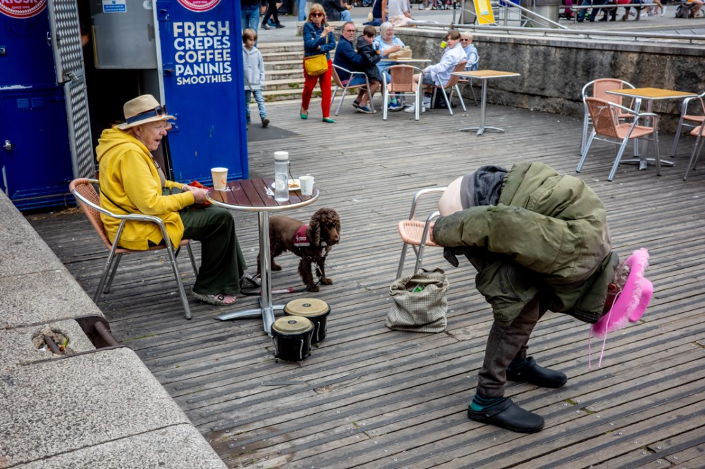 Candid street photography of a dog watching a man pull a moonie in Bristol, UK.