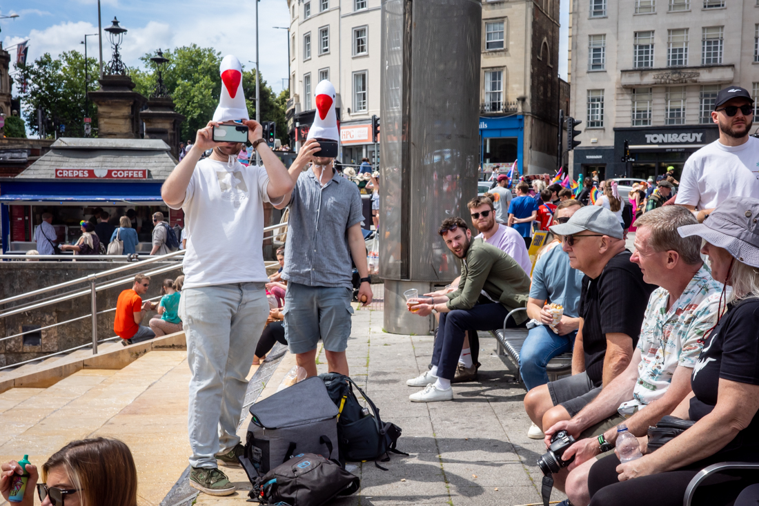 Candid street photography of men in swan hats taking photos in Bristol.