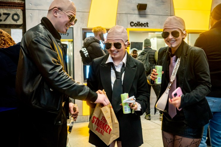 People with fake bald heads in London Waterloo station. Candid street photography by Darren Lehane