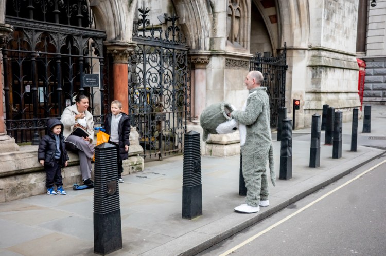 A family look at a man in a fancy dress costume on Fleet Street in London. Candid street photography by Darren Lehane