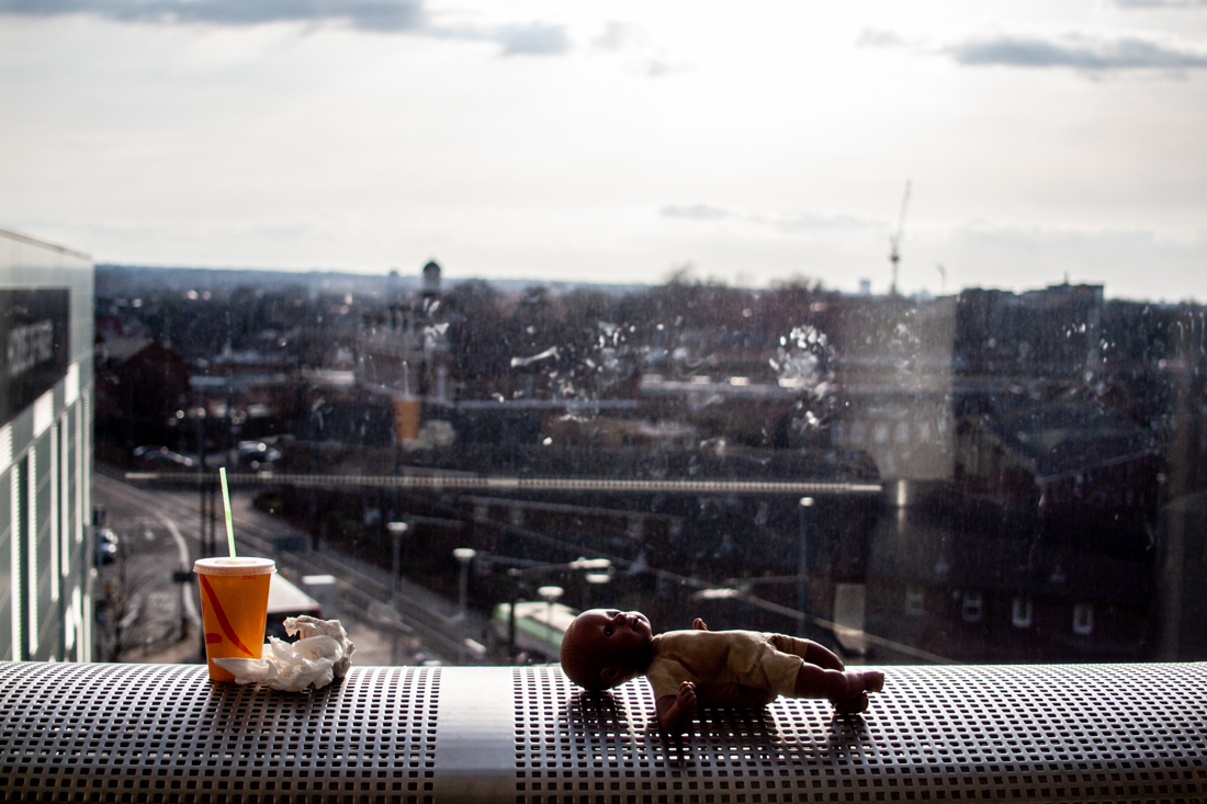 Candid street photography of a discarded doll on a bench, with Croydon in the background.