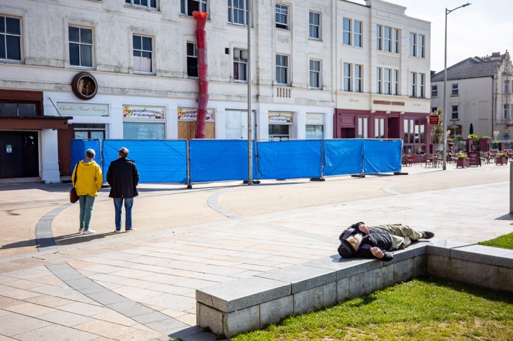 A couple stand oblivious with backs to sleeping man in Weston-super-Mare.