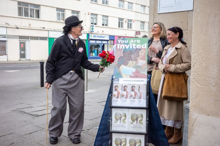 Candid street photography of man dressed as Charlie Chaplin, handing flowers to two Jehovah Witness in Weston-super-Mare.