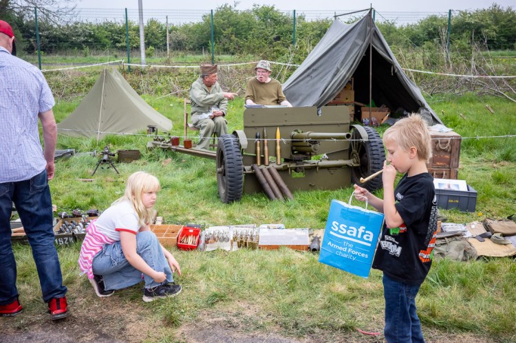 Candid street photography of a boy blowing on a party blowers in front of an army tent in Weston-super-Mare.