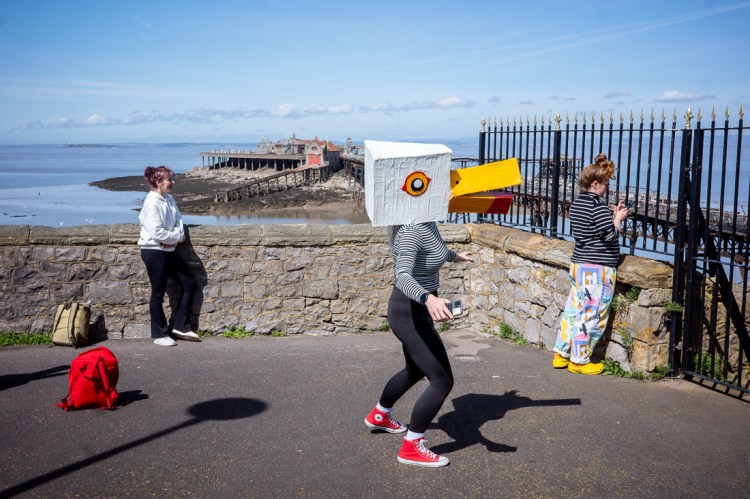 Candid street photography of a girl with a cardboard seagull head in Weston-super-Mare.
