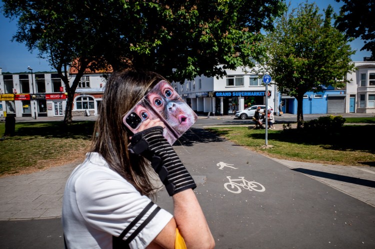 Candid street photography of a woman with a monkey face on her phone, in Weston-super-Mare