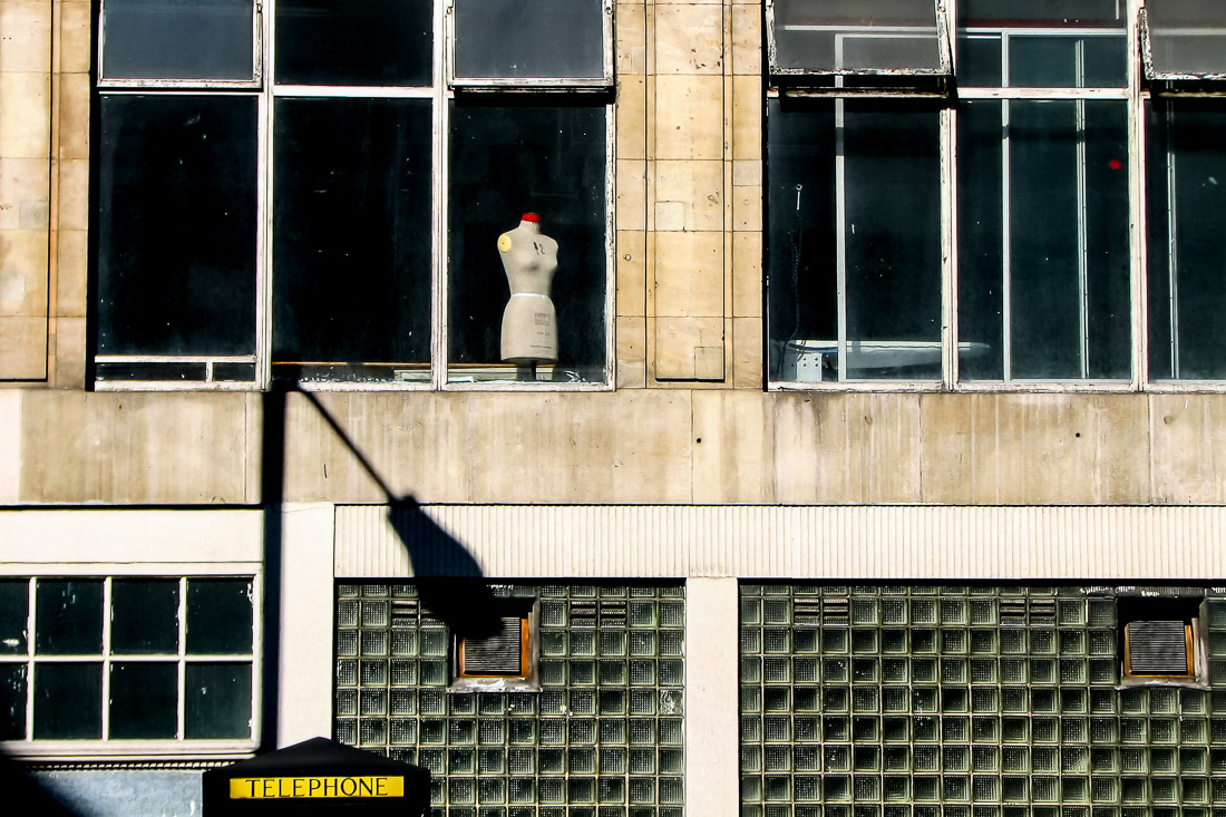 Candid street photography taken in the City of London on 13 July 2008, featuring a solitary mannequin in a window above a brutalist building facade, evoking themes of loneliness and urban isolation.