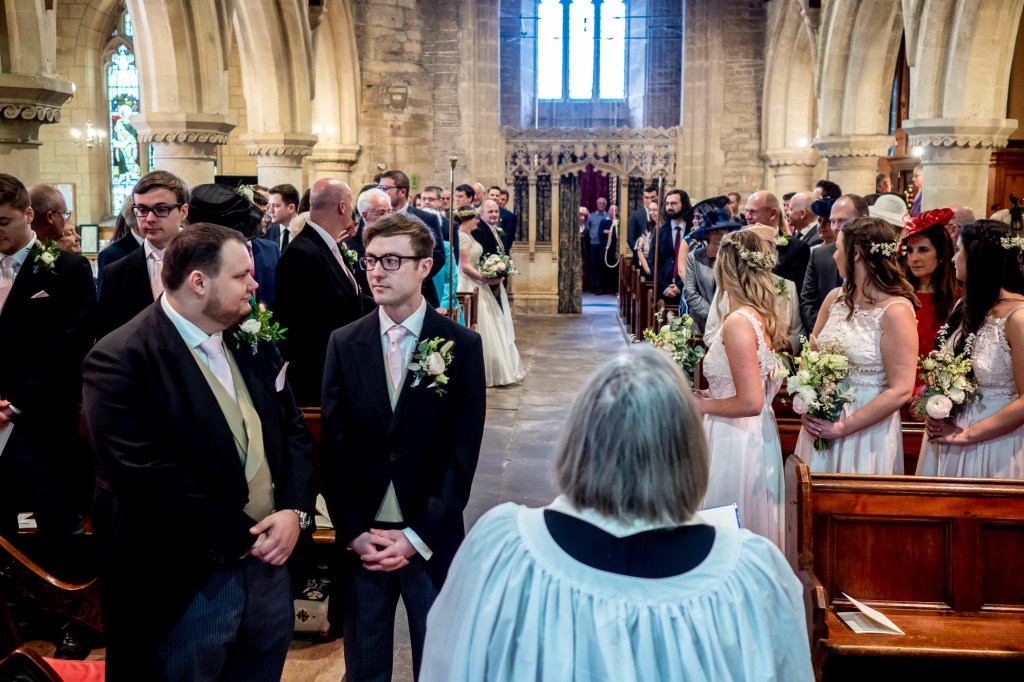 The groom looks at his best man, as the bride comes up the aisle at Grittleton House in Wiltshire.