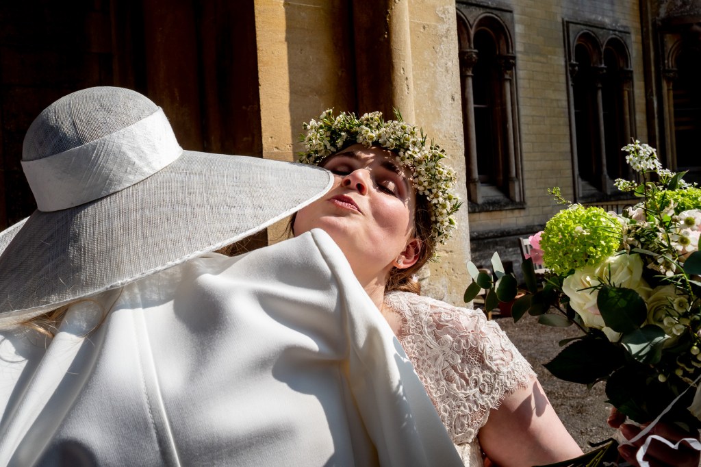 The bride air kisses a guest, in a large wedding hat, at Grittleton House in Wiltshire.
