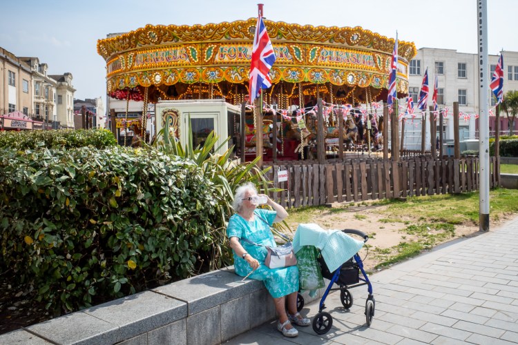 Candid street photography of an old woman with a plastic glass to her face in Weston-super-Mare.