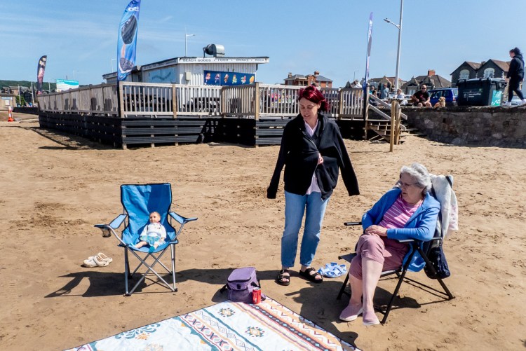 Candid street photography of a doll sat in a chair on the beach in Weston-Super-Mare.