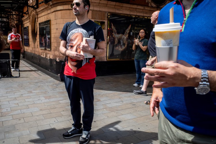 Candid street photography of a man with a large face on his T shirt, on Cambridge Circus in London.