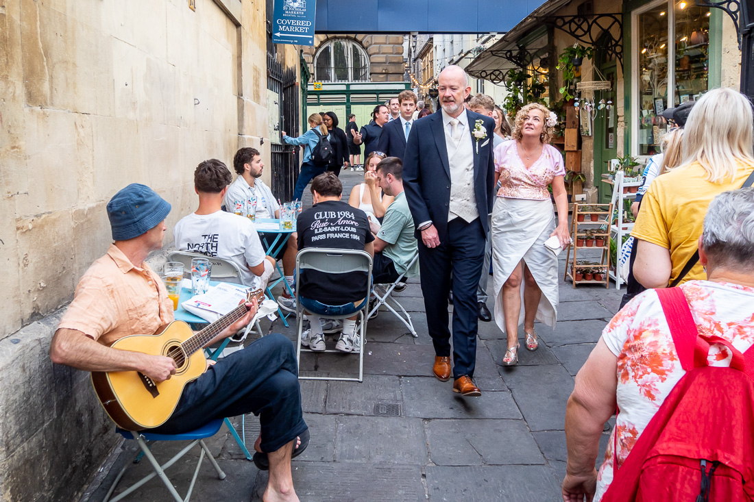 The bride and groom walk past a guitarist during a Bristol wedding day.
