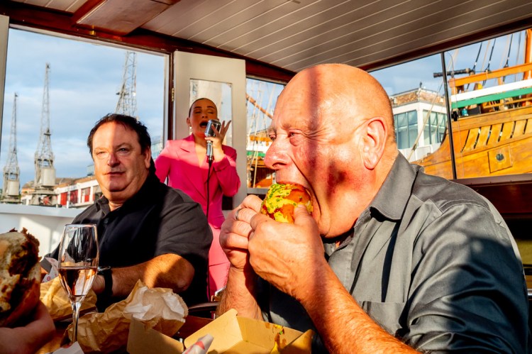 A guest eats a hot dog, as the wedding singer performs in the background, during a Bristol wedding on the Flower of Bristol boat, run by Bristol Packet tour company.
