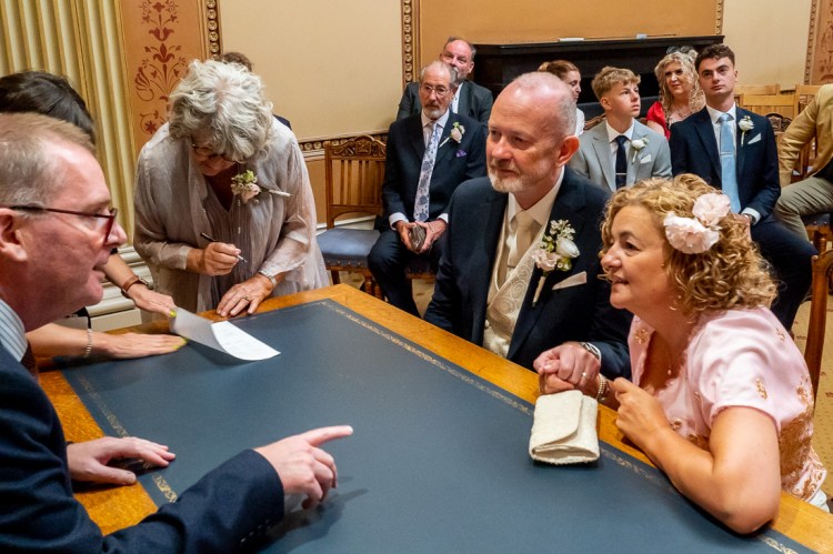 The bride and groom watch a witness sign the register during a wedding at Bristol Register Office in Bristol.