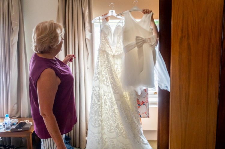 Mother-of-the-bride holds up dresses, during the bridal preparations of a wedding at Worcester College in Oxford.