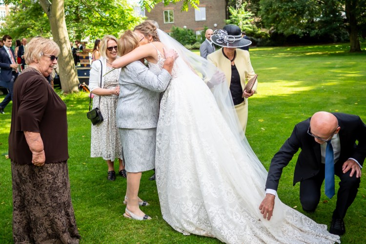 The bride hugs a guest, as a male guest adjusts her dress, during a wedding at Worcester College in Oxford.