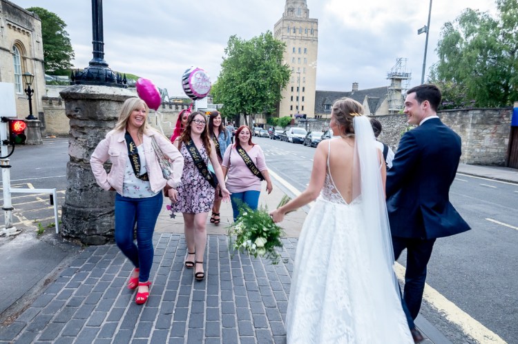 The bride and groom pass a hen party during a wedding day in Oxford.