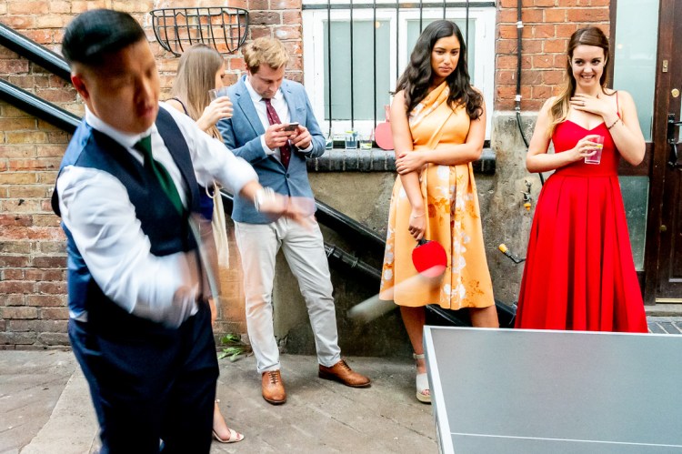 Guests watch a groomsman playing ping pong at the Jam Factory during a wedding in Oxford.