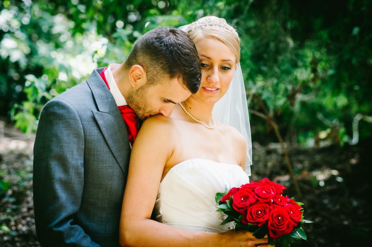 A formal wedding portrait of the groom kissing the bride's shoulder, during a wedding as Sedgebrook Hall in Northamptonshire.