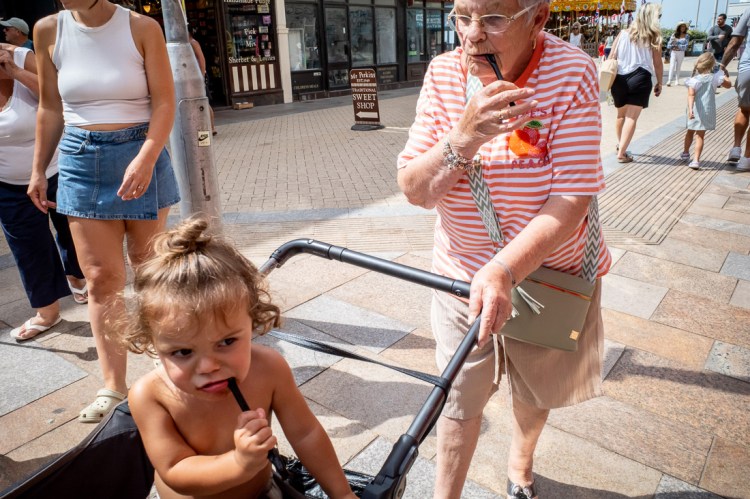 Candid street photography of a boy and old lady chewing on a liquorice stick in Weston-super-Mare, North Somerset, UK.