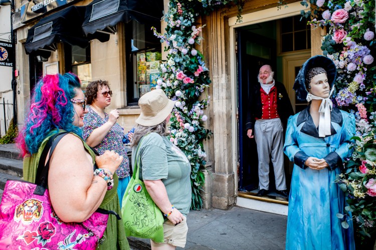 Candid street photography of tourists and a man in period costume, outside the Jane Austen museum in Bath, North Somerset, UK.