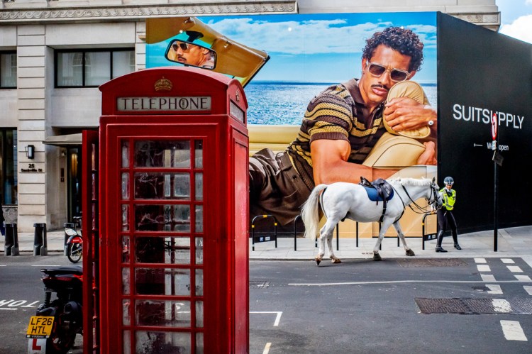 Candid street photography of a police horse in front of a large man on an advertising board in London, UK