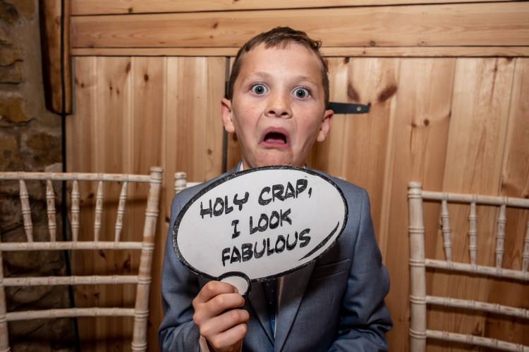 A young guest with a sign that says "Holy crap I look fabulous" during a wedding at the Barns at Hunsbury Hill in Northampton.