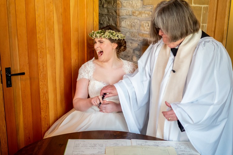 The bride laughs as she signs the wedding register, during a wedding at Grittleton House, in Wiltshire