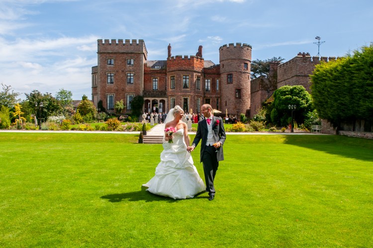 The bride and groom stroll hand in hand across the lawns, during a wedding at Rowton Castle in Shropshire.