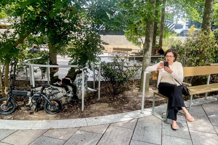 Candid street photography of a woman on phone and children playing in a bush in Croydon, London.