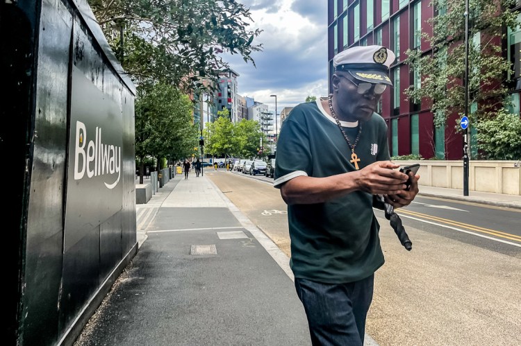 Candid street photography of a man with cross and sailors hat in Croydon, London