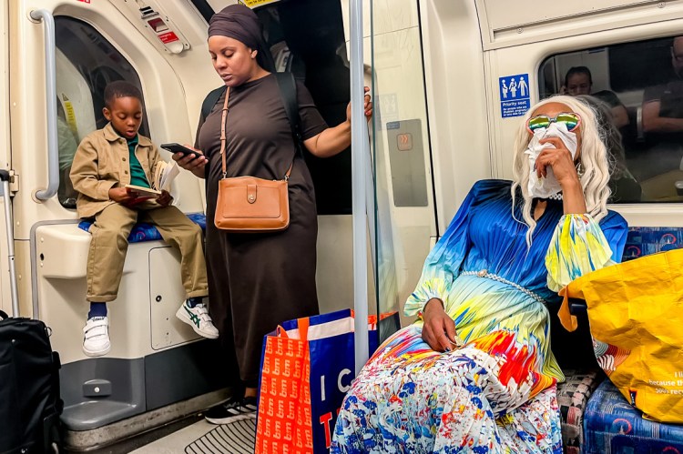 Candid street photography of a woman with a hanky and colourful dress on the Tube in London.